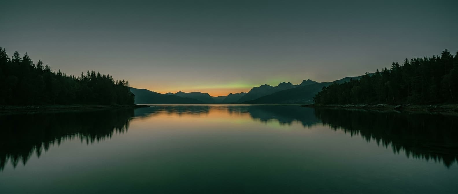 Stiller Fjord in der Abenddämmerung mit Nordlicht am Horizont