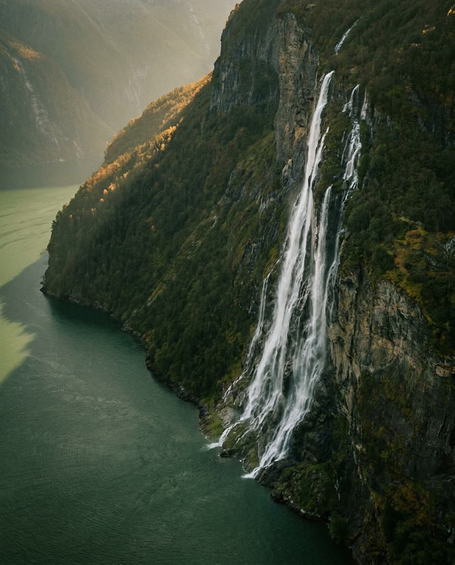 Ein hoher Wasserfall stürzt in einen grünen Fjord